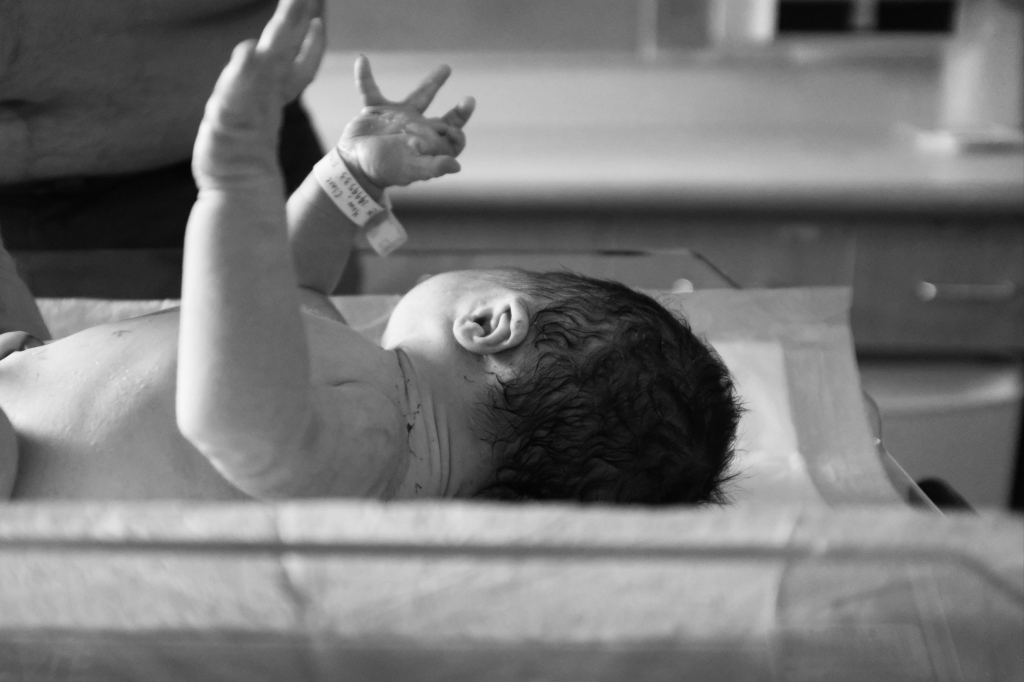 A newborn baby laying on a weigh scale with arms outstretched. 