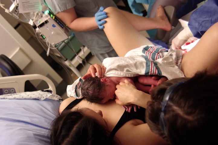 A mother reclined in a hospital bed with new born baby on chest. 
